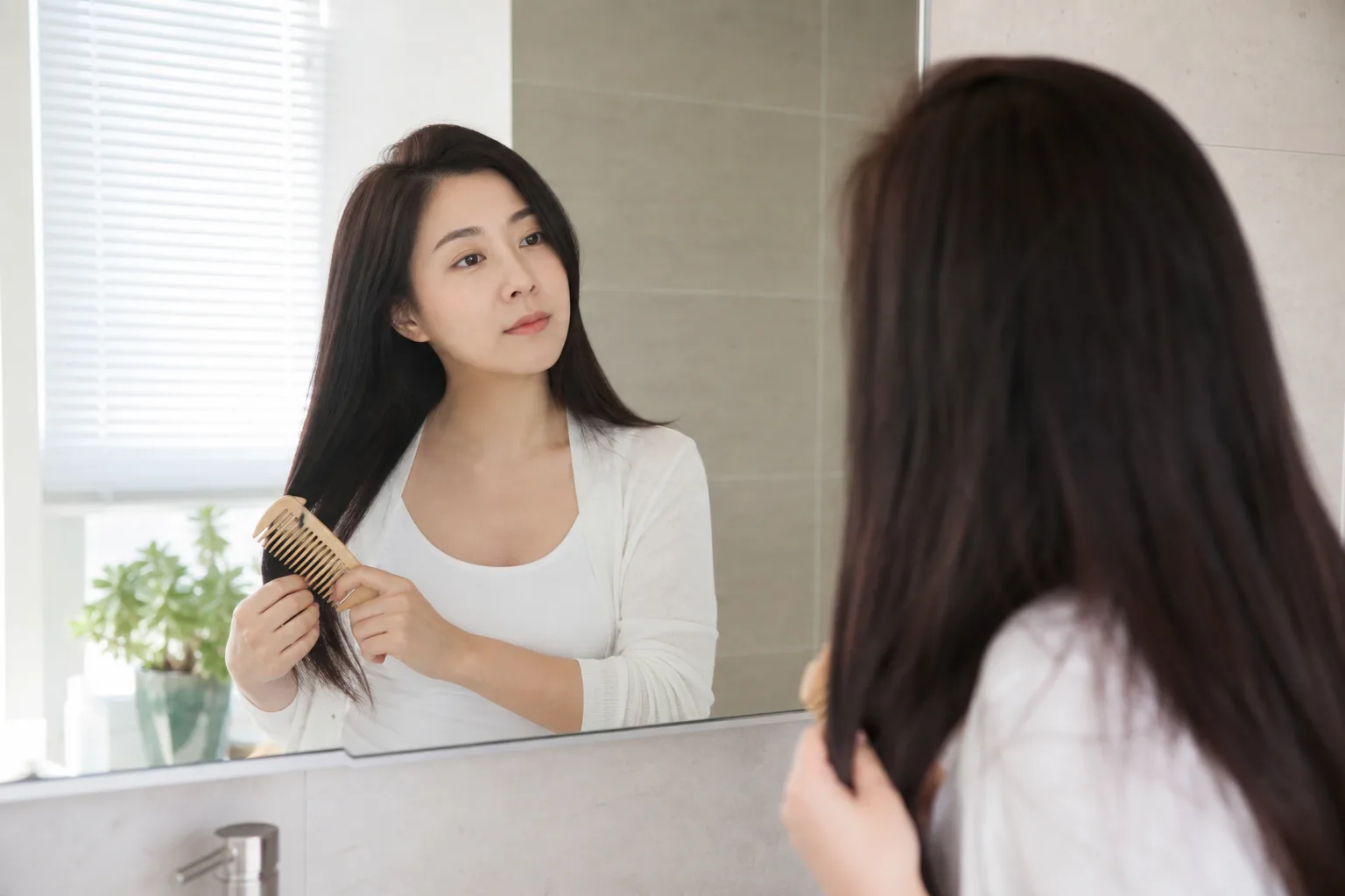여성이 거울 앞에서 넓은 빗으로 머리카락을 부드럽게 관리하는 모습